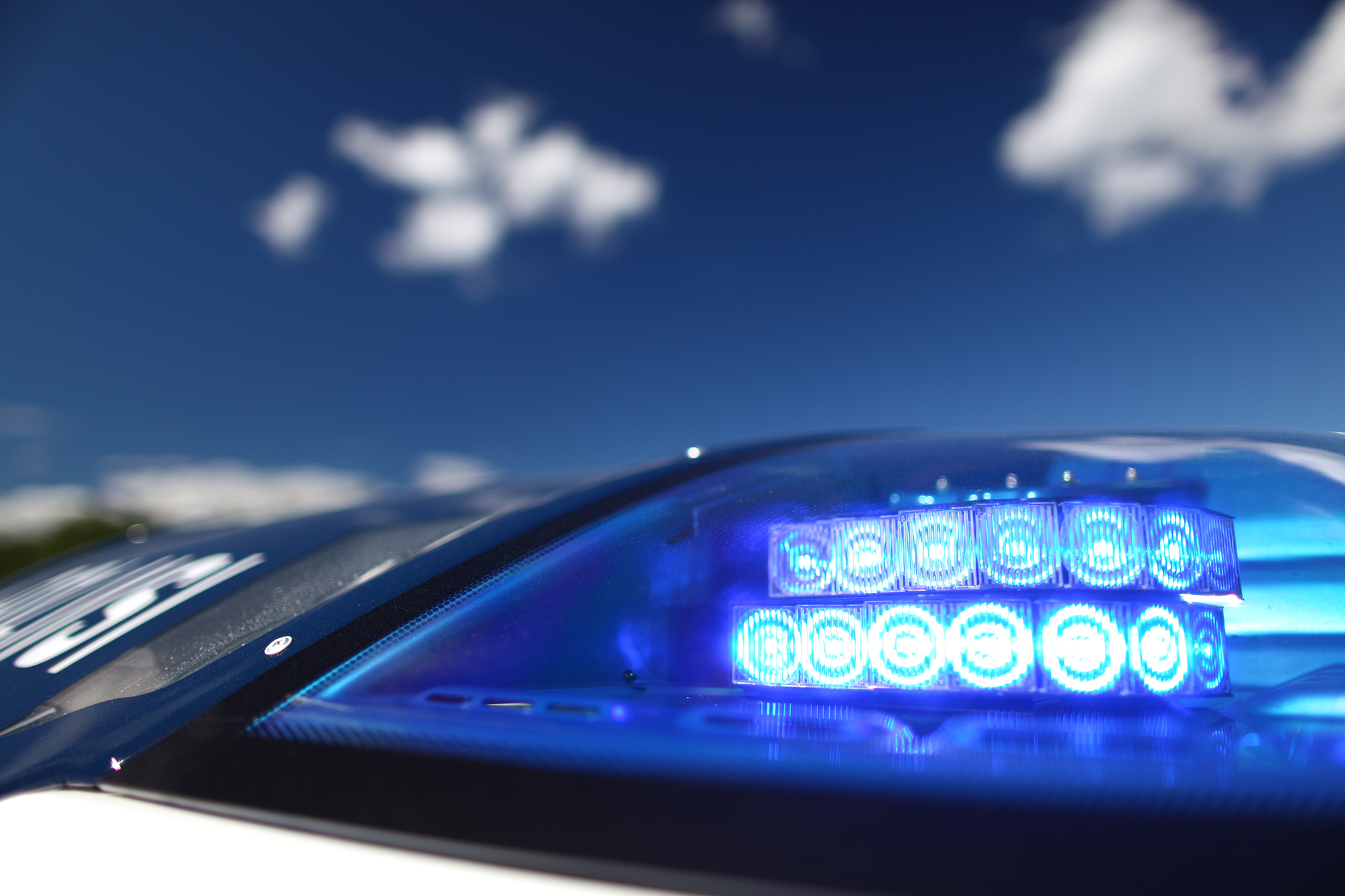A close-up image of a police car’s flashing light, with blue sky in the background.